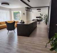 Kitchen and living room in a family house with an island, a yellow sofa, and a floor with a wooden decor.