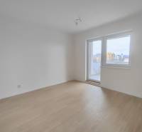 An empty room in a two-room apartment with a wood-patterned floor and balcony doors.