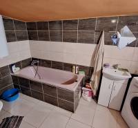 A bathroom in a family house with a bathtub, washing machine, and electric boiler.