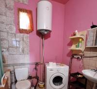 A bathroom in a family house with a washing machine, toilet, and pink walls.