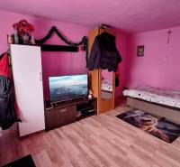 A pink room in a family house with beds, a television, and a wooden decor floor.