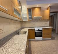 A kitchen with wooden cabinets and wallpaper in a 3-room apartment, flooring with a wooden decor.