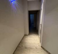 A hallway with a wood-patterned floor, lighting, and white walls in a 3-room apartment.