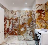 A bathroom in a 3-room apartment with onyx tiles, a glass-enclosed shower, and a washing machine.