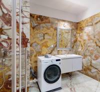 Luxury bathroom in a 3-room apartment with marble tiles, a shower, and a washing machine.