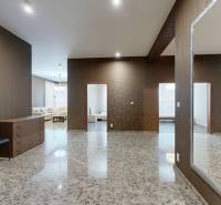A spacious hallway with tiles, a mirror, two chairs, and a view into the living room.