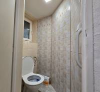 A bathroom in a one-room apartment with a toilet tiled in beige tiles.
