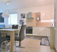 A modern kitchen with a dining table, white cabinets, and a wood-decor floor in a two-room apartment.