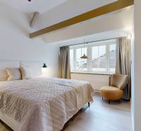 A bedroom with a light wood-patterned floor, a large window, and a comfortable chair.