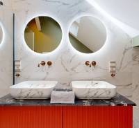 A bathroom with double sinks, a marble wall, and round mirrors in a 4-room apartment.