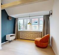 A room in a 4-room apartment with an orange armchair, light wood-patterned flooring, and a large window.