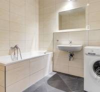 Bathroom with a bathtub, sink, and washing machine in a 3-room apartment. Walls with beige tiles.