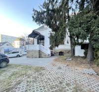 Building on Vajanského in Prešov with an access road, cars, and spruces in the foreground.