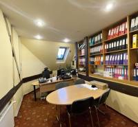 An office in a building with a slanted ceiling, desks, and shelves with documents.