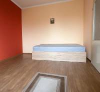 A room in a family house with a wooden decor floor, a bed, and a red wall.