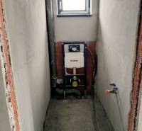 Construction preparation for a toilet in a family house with a built-in tank, white walls, and a small window.