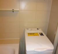 Bathroom in a 2-room apartment with a washing machine next to the bathtub and shelves.