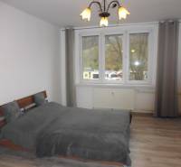 Bedroom in a 2-room apartment with a bed and wooden decor flooring, gray curtains.