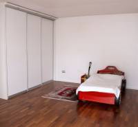 Children's room in a family house with a car-shaped bed and a wooden-patterned floor.