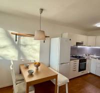 A kitchen in a 3-room apartment with a wooden decor floor, a dining table, and appliances.