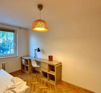 A room in a 3-room apartment with a wooden decor floor, a desk, and a lamp.