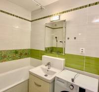 A bathroom in a three-room apartment, with green tiles, a bathtub, a sink, and a washing machine.