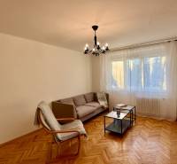 Living room with a sofa, armchair, chandelier, and wood-patterned flooring in a 3-room apartment.