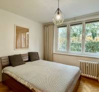 A bedroom with wood-patterned flooring, a bed, and a large window in a three-room apartment.