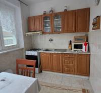A kitchen in a 3-room apartment with a kitchen unit, stove, microwave, and table with a tablecloth.