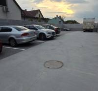 Parking lot on Banka Street in Piešťany with cars and a truck at sunset.