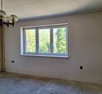 A room in a family house with a large window, an original chandelier, and a view of greenery.