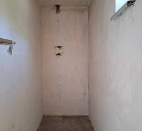 A narrow interior space in a family house with a small window and a concrete floor.