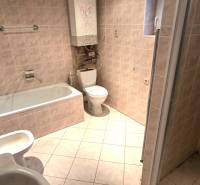 Bathroom in a family house with a bathtub, sink, and toilet. Light-colored tiles.