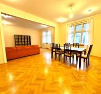 Dining room with a set of tables and chairs, next to the living room with an orange sofa. Floor with wooden decor.