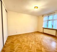 A room in a 4-room apartment with a large window, white walls, and a floor with a wood decor.