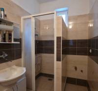 A bathroom with a sink and a shower, decorated in light-toned tiles.