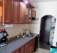 A kitchen in a 3-room apartment with wooden cabinets and a tiled wall above the countertop.