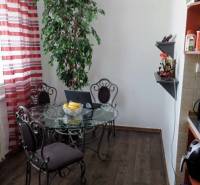 Dining room in a 3-room apartment with a glass table, potted plant, and wood-patterned flooring.