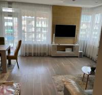 Living room in a four-room apartment with a wooden decor floor and a television on the wall.