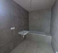 A bathroom with large-format gray tiles, a sink, and a bathtub in a family house.
