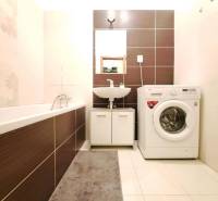 A bathroom in a 2-room apartment with a washing machine, bathtub, and sink.