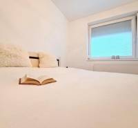 A view of a bed with an open book and a window in a 2-room apartment.