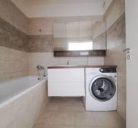 Bathroom in a 2-room apartment with a bathtub, washing machine, and beige tiles.