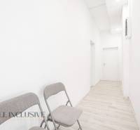 White office walls with two folding chairs, a narrow corridor, and closed doors.