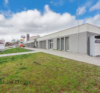 On Vajanského Street, there are commercial spaces, and next to the sidewalk, there is a green lawn.