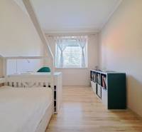 A room in a family house with a bed, a bookshelf, and a wooden-patterned floor.