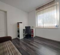 A room in a family house with a wooden decor floor, a table, a chair, and a sofa.