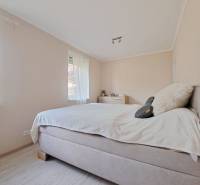 A bright bedroom in a family house with a comfortable bed and a wooden-patterned floor.