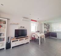 Living room in a family house with a television, kitchenette, and a table with three chairs.
