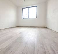 A room in a family house with a wooden decor floor, white walls, one window.